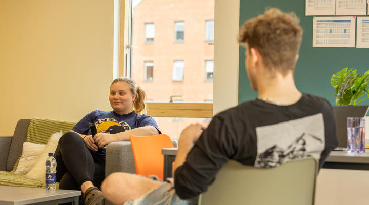 Blackfriars living space, a male and female student sat opposite chatting