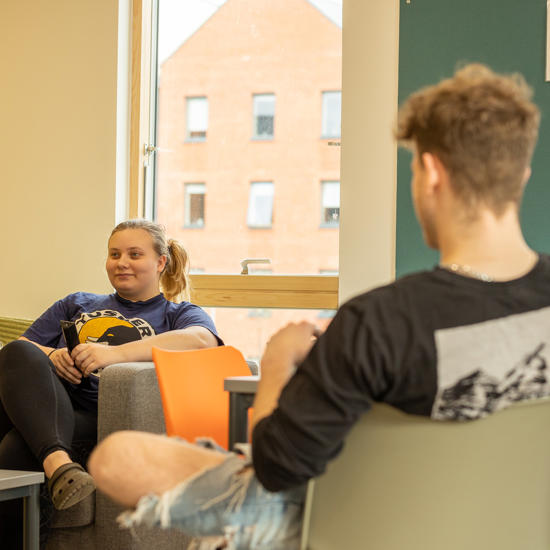 Blackfriars living space, a male and female student sat opposite chatting