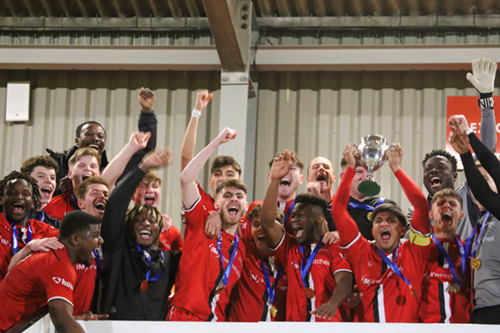 A group of football players in red and black uniforms holding a trophy and celebrating